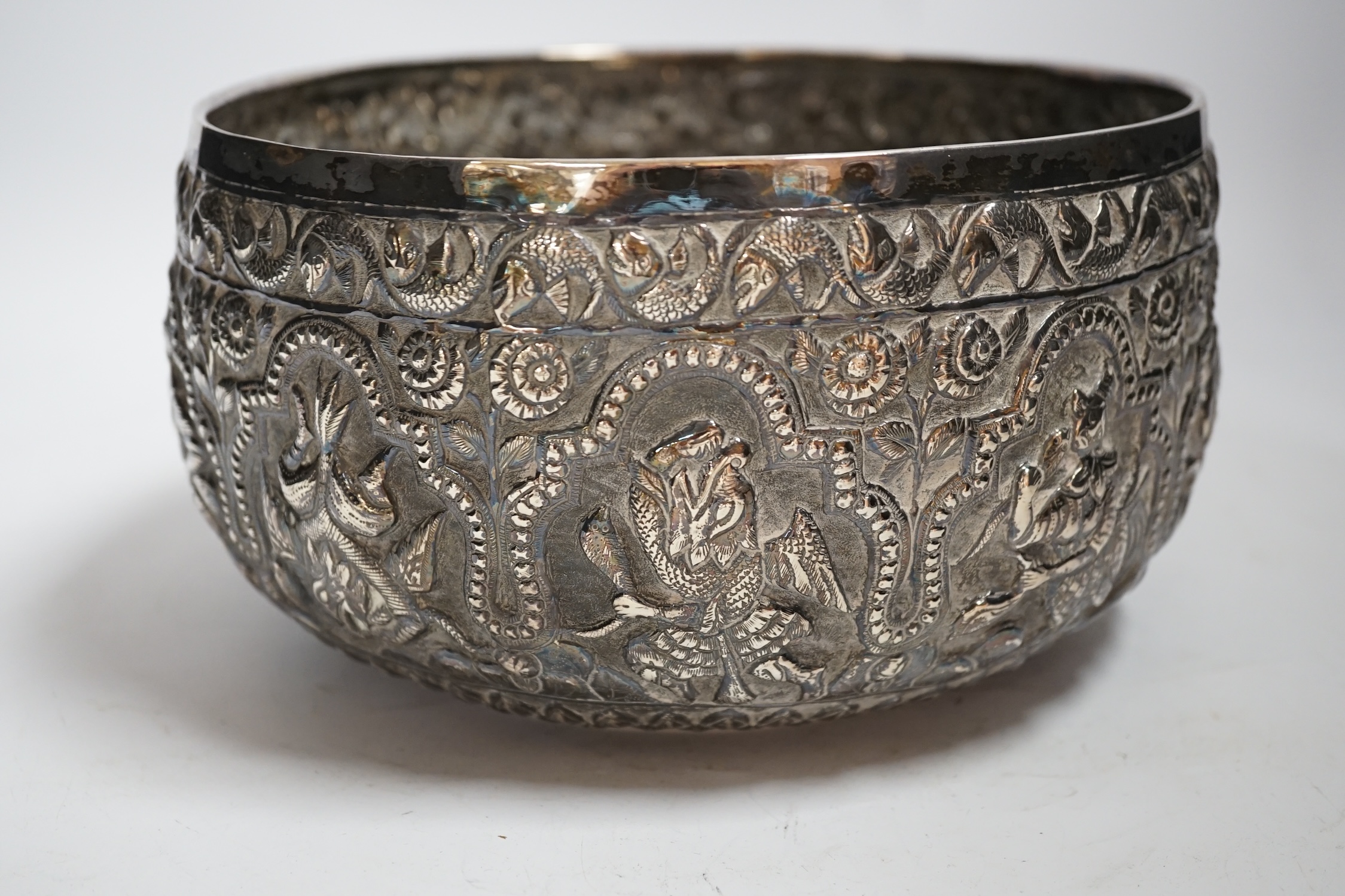 A 19th century Burmese embossed white metal bowl, decorated with figures and flowers, diameter 22.2cm, 22.9oz.